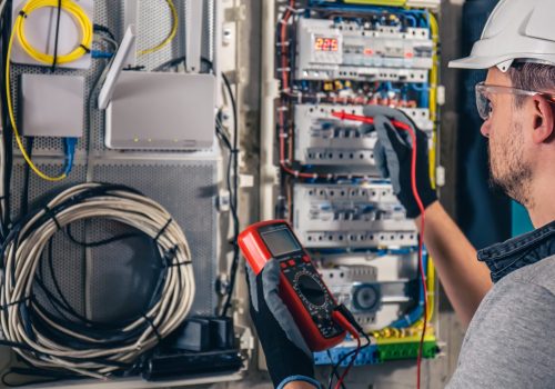 Man, an electrical technician working in a switchboard with fuses. Installation and connection of electrical equipment. Professional uses a tablet.